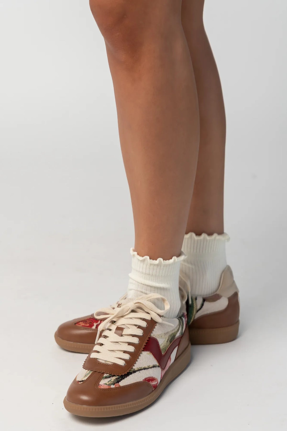 Pair of low-top sneakers  featuring cognac faux leather overlays, floral tapestry panels with rose motifs, and cream laces. The vintage-inspired design combines mixed textures and warm tones for a casual yet elevated everyday look.