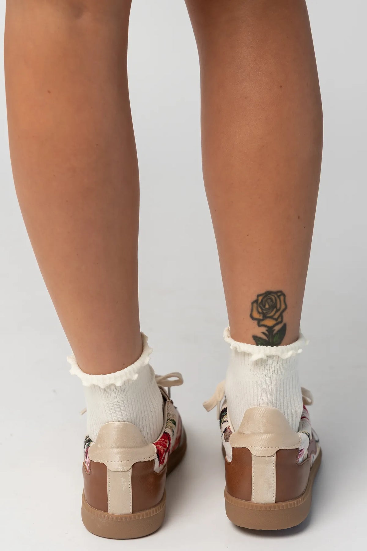 Pair of low-top sneakers  featuring cognac faux leather overlays, floral tapestry panels with rose motifs, and cream laces. The vintage-inspired design combines mixed textures and warm tones for a casual yet elevated everyday look.