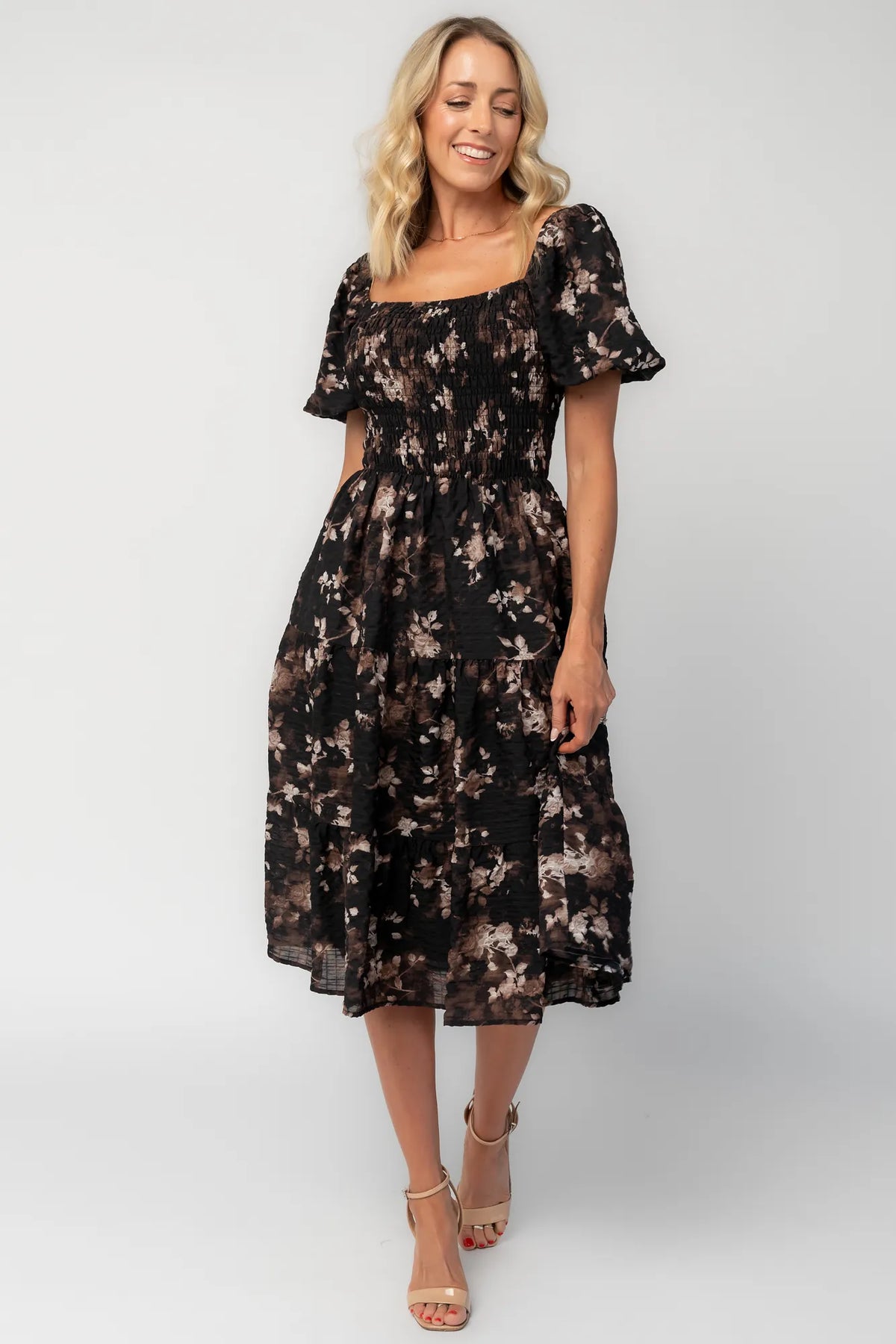 Model wearing a midi dress with a fully smocked bodice, square neckline, and short balloon sleeves.