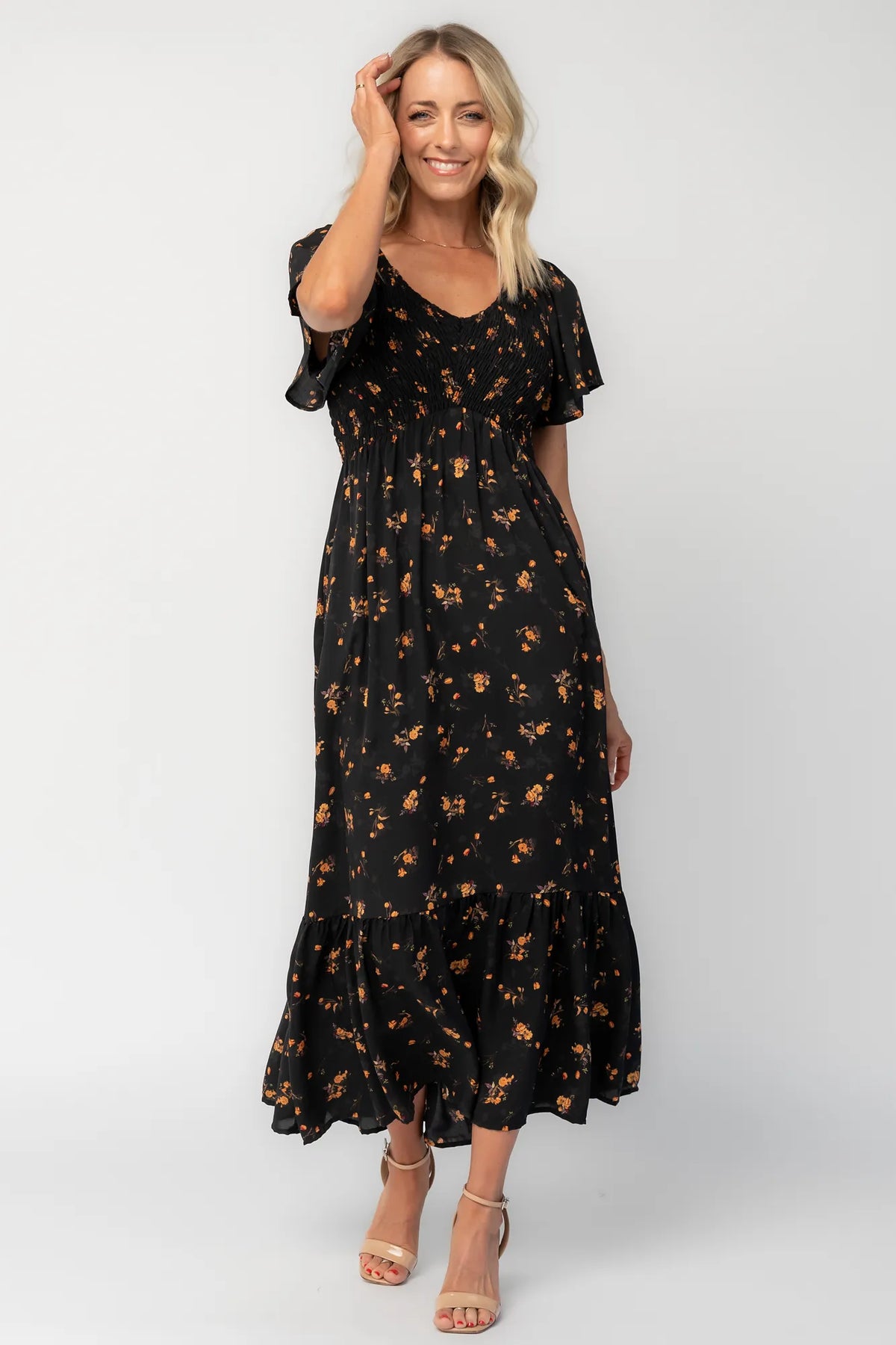 Model wearing a floral midi dress with a smocked bodice, wide V-neckline, and flutter sleeves.