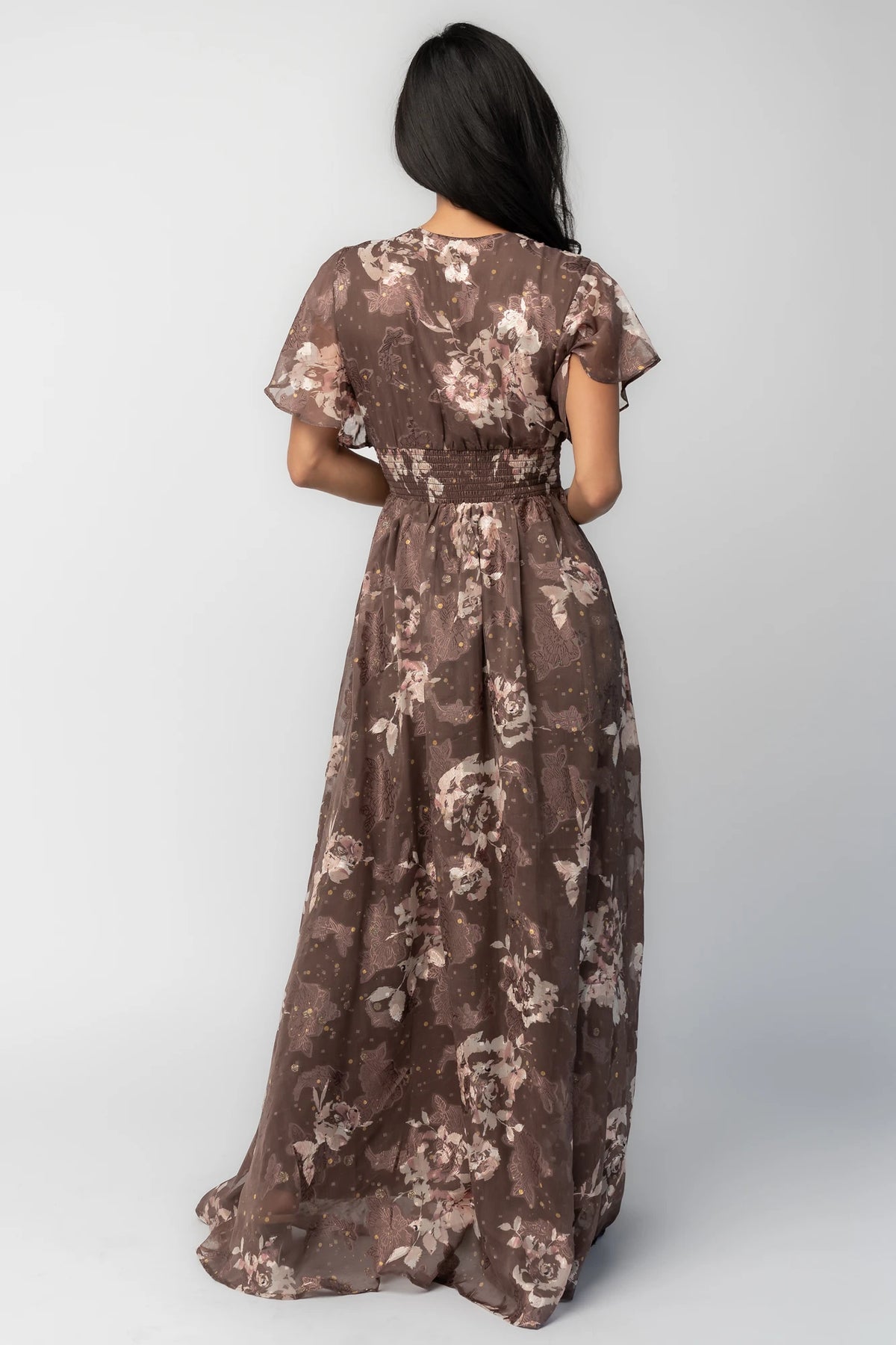 Mocha metallic floral chiffon maxi dress with a V-neckline, flutter sleeves, smocked waist, and flowing full-length skirt.