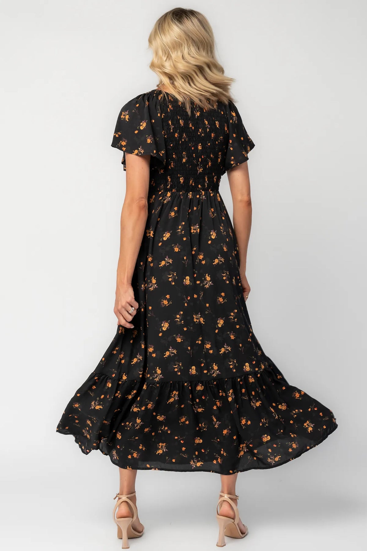 Model wearing a floral midi dress with a smocked bodice, wide V-neckline, and flutter sleeves.