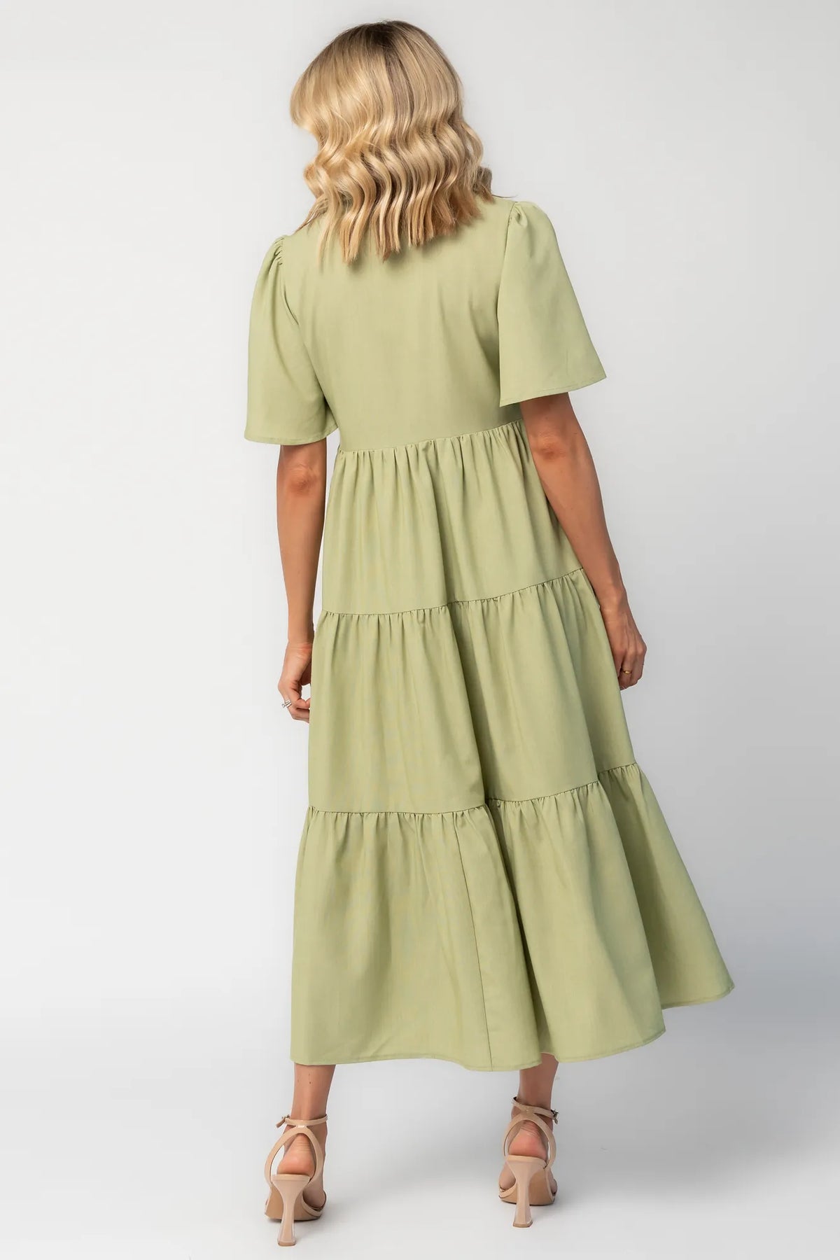 Model wearing a sage green midi dress with a collared neckline, button-front bodice, and short flutter sleeves.
