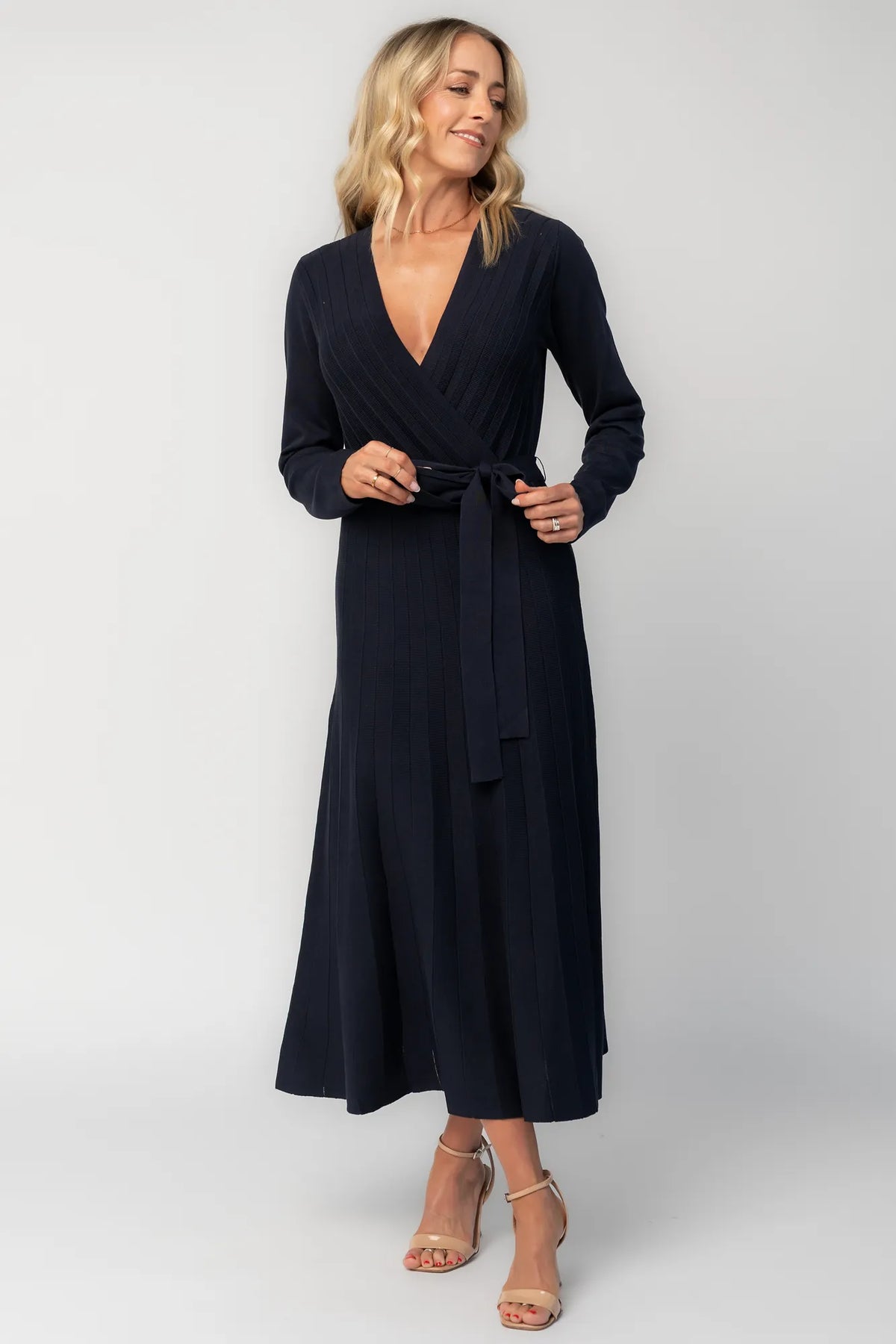 Model wearing a navy midi dress with a surplice V-neckline, long sleeves, and a matching waist tie