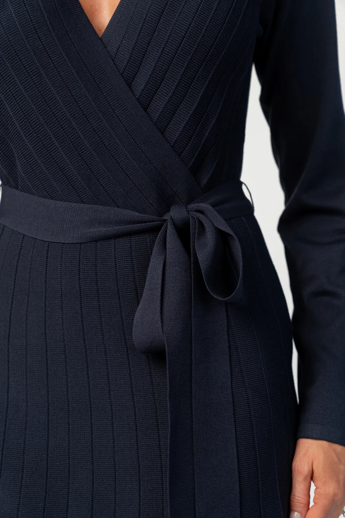 Cropped image of model wearing a navy midi dress with a surplice V-neckline, long sleeves, and a matching waist tie