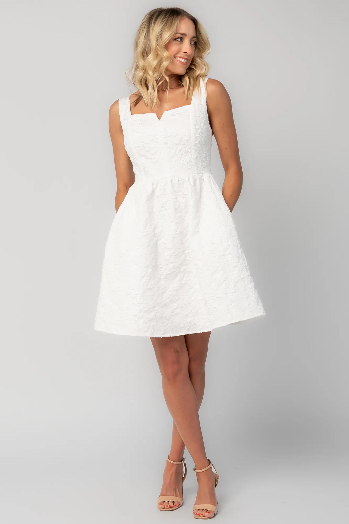 Model wearing an ivory sleeveless mini dress with a square neckline and subtle notch detail.