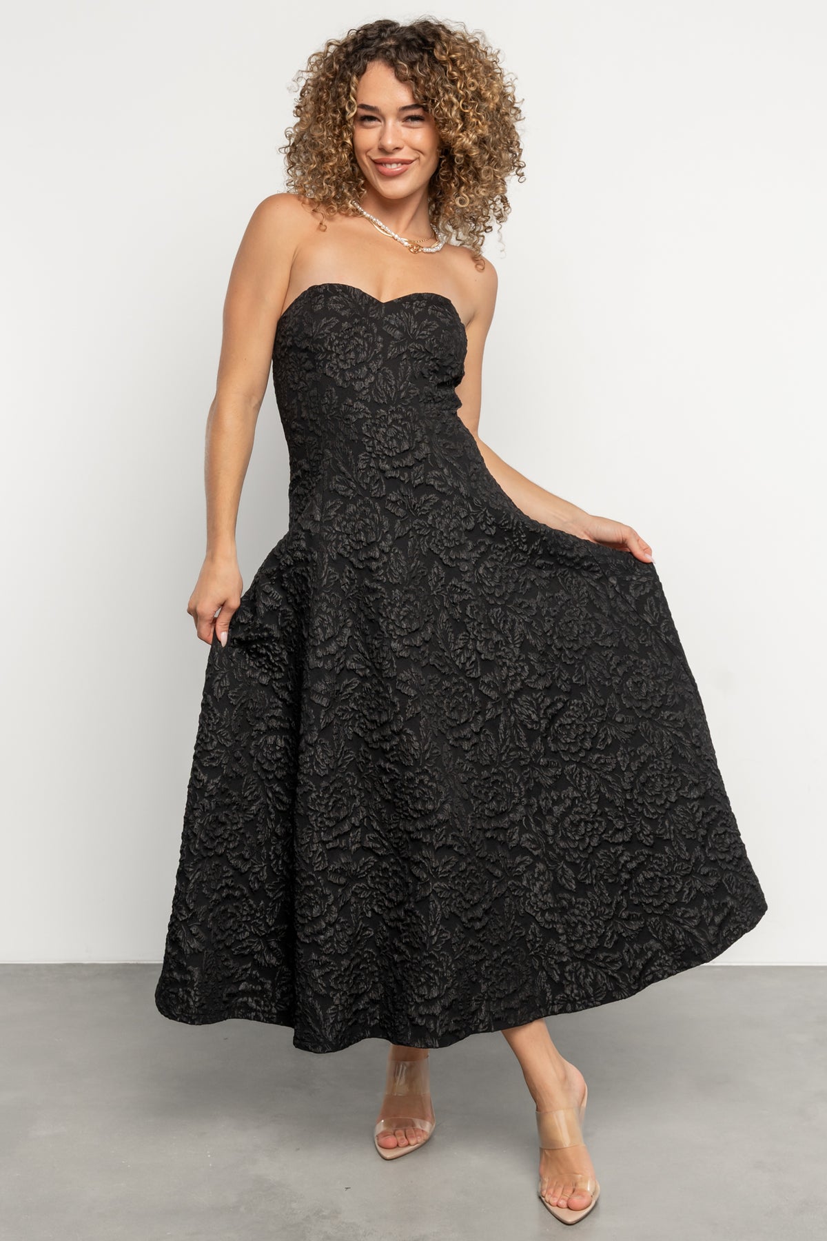 Front view of model wearing Selene strapless midi dress in black, showing embossed floral texture and sweetheart neckline.