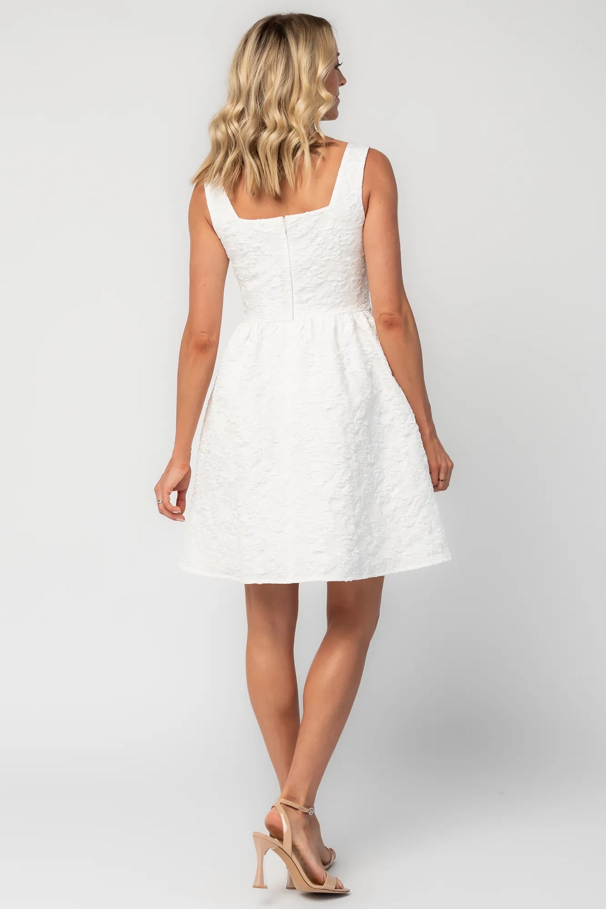 Model wearing an ivory sleeveless mini dress with a square neckline and subtle notch detail.