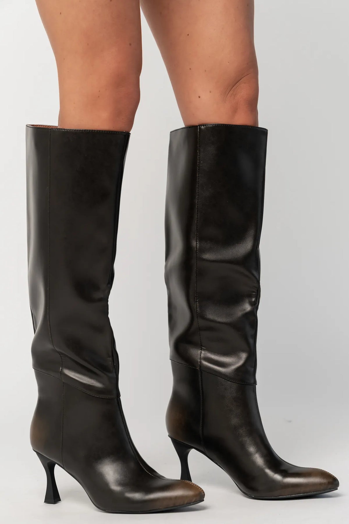 Pair of black knee-high boots featuring a pointed toe, sleek fitted shaft, and sculpted kitten heel. The streamlined silhouette and smooth finish create an elegant, versatile look that pairs effortlessly with dresses, skirts, and tailored outfits.