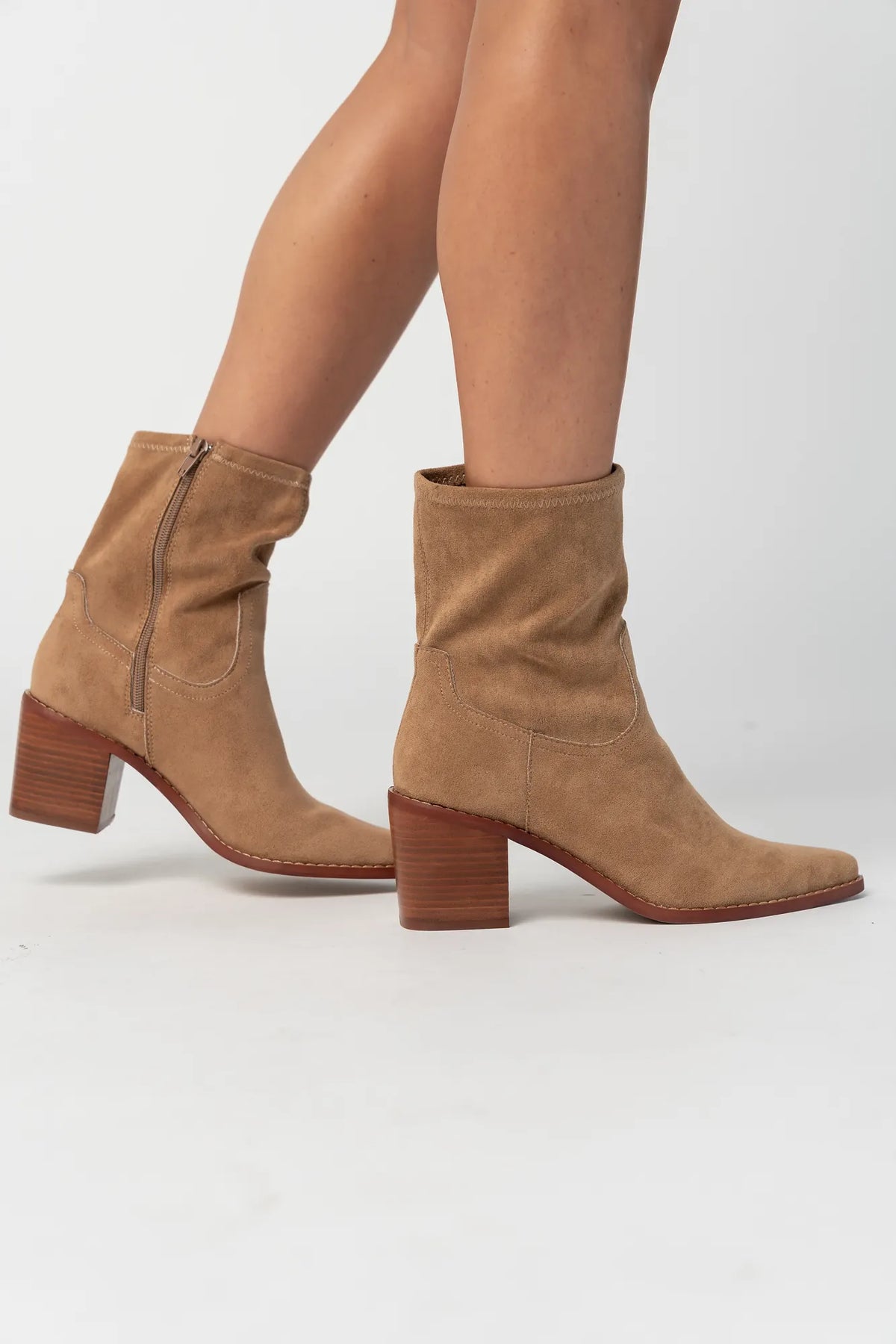Pair of sand-colored ankle boots featuring a soft suede-like finish, pointed toe silhouette, and stacked block heel. The boots include a side zipper closure and subtle western-inspired seam detailing, creating a versatile look that pairs easily with denim, dresses, and seasonal outfits.
