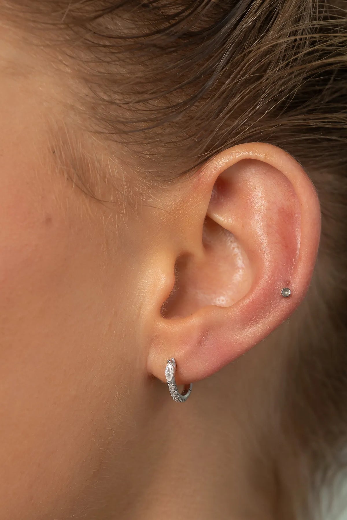 Model wearing petite sterling silver huggie hoop earrings featuring a marquise-cut crystal accent and a row of sparkling stones along the front. 