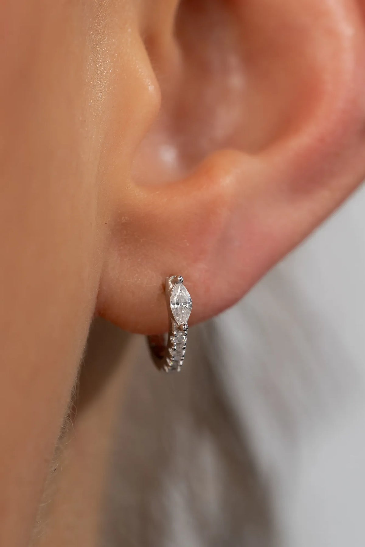 Model wearing petite sterling silver huggie hoop earrings featuring a marquise-cut crystal accent and a row of sparkling stones along the front. 