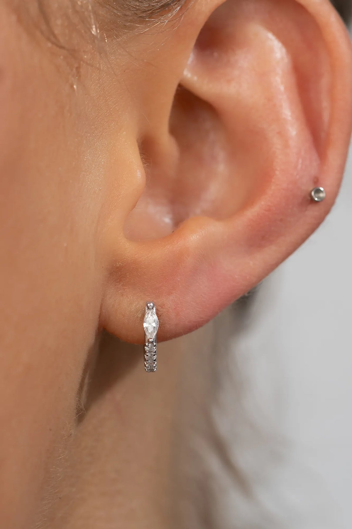 Model wearing petite sterling silver huggie hoop earrings featuring a marquise-cut crystal accent and a row of sparkling stones along the front. 