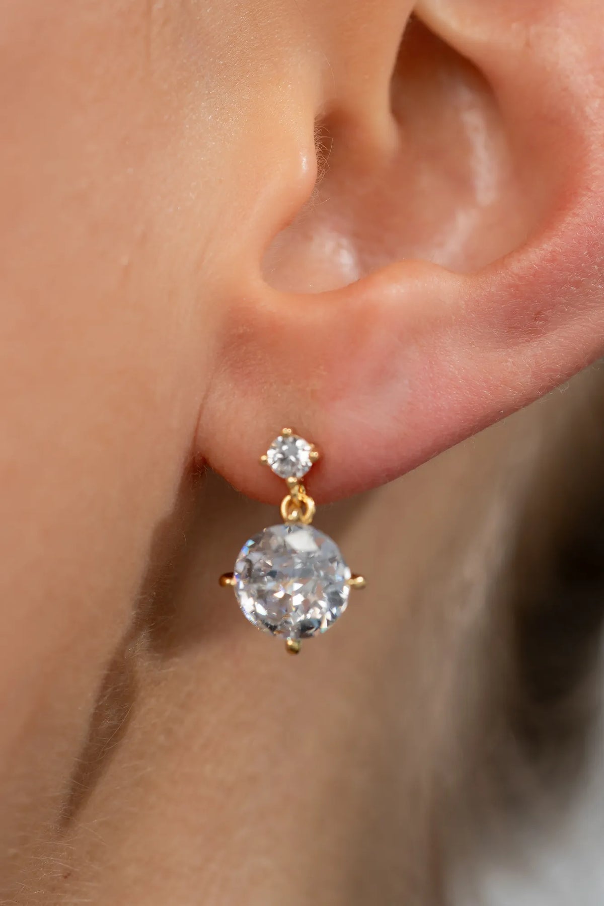 Model wearing gold-tone drop earrings featuring sparkling round zircon stones suspended from petite stud tops.
