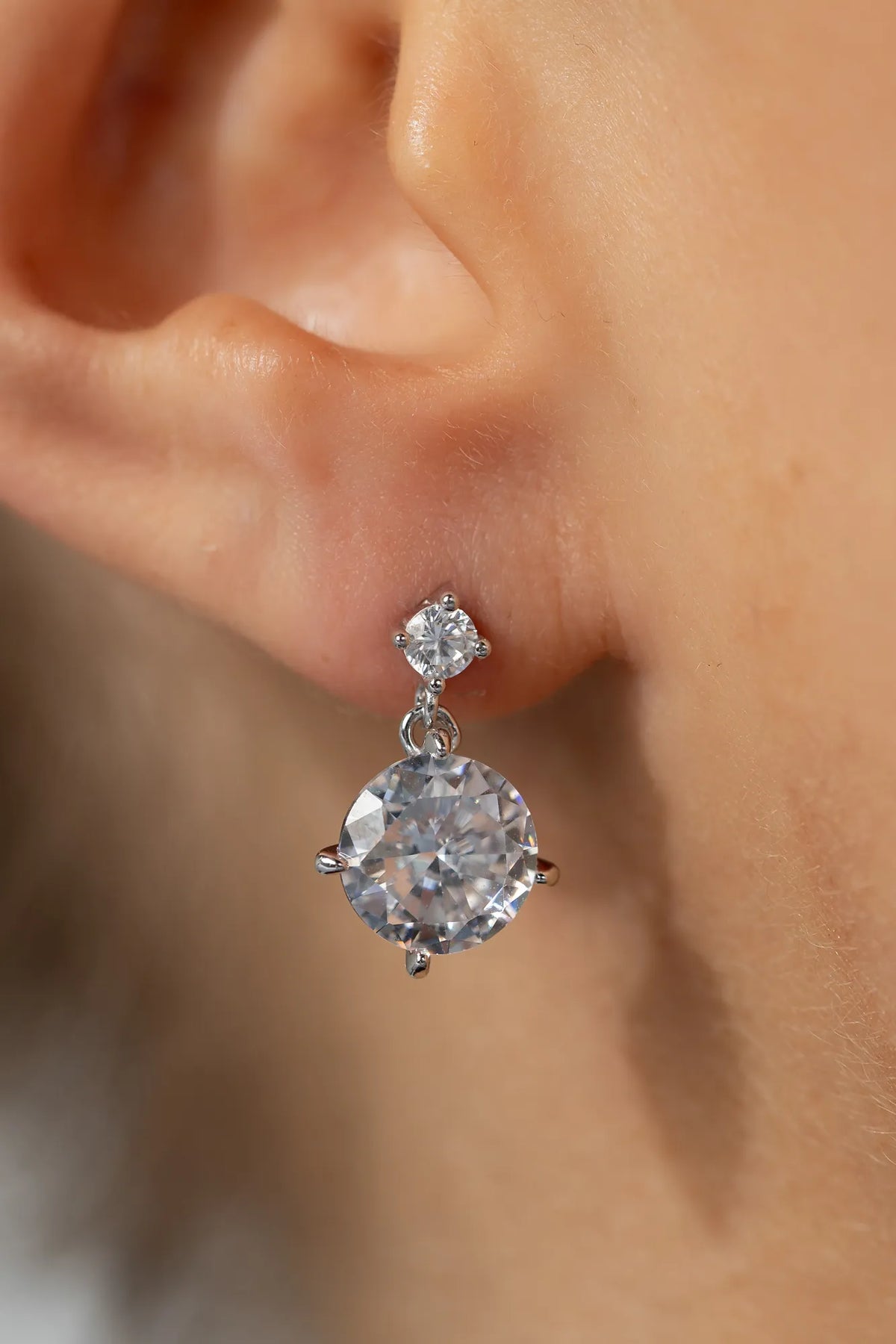 Model wearing silver-tone drop earrings featuring sparkling round zircon stones suspended from petite stud tops.