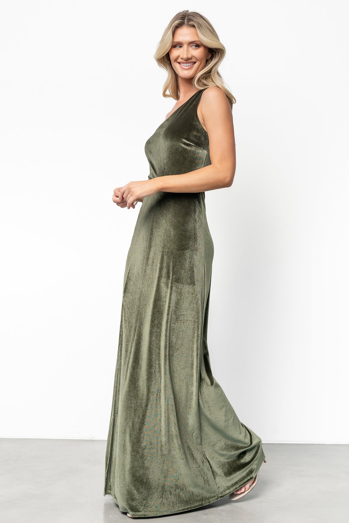 Studio shot of olive velvet maxi dress on a form, showing fabric texture, asymmetrical neckline, and mid-thigh slit for movement and style.
