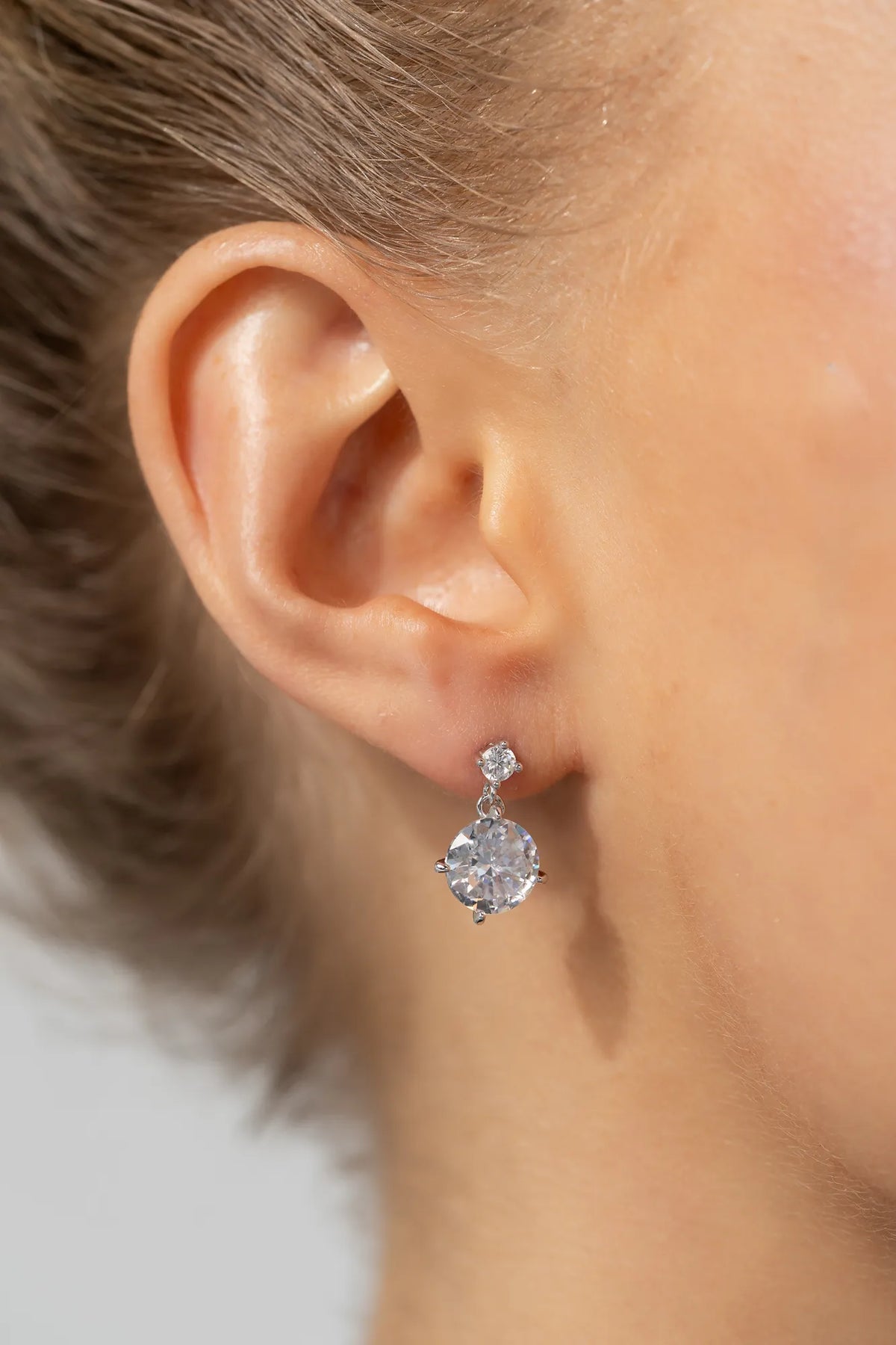 Model wearing silver-tone drop earrings featuring sparkling round zircon stones suspended from petite stud tops.