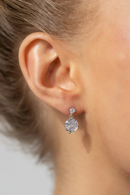 Model wearing silver-tone drop earrings featuring sparkling round zircon stones suspended from petite stud tops.