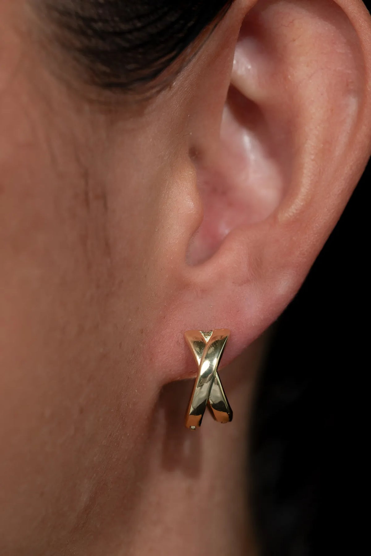 Model wearing gold-tone huggie earrings with a polished finish, sitting close to the earlobe.