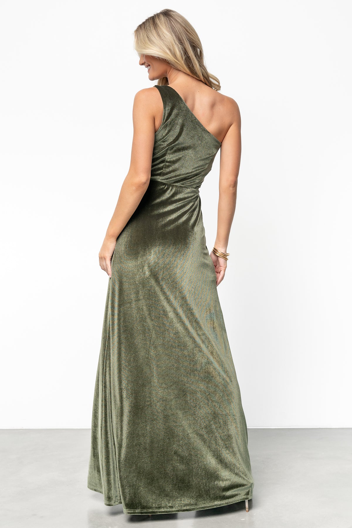 Side view of olive velvet maxi dress featuring the asymmetrical single-shoulder silhouette, gentle skirt flare, and right-side slit to mid-thigh.