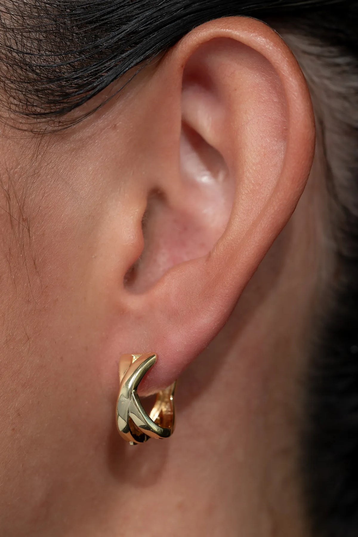 Model wearing gold-tone huggie earrings with a polished finish, sitting close to the earlobe.