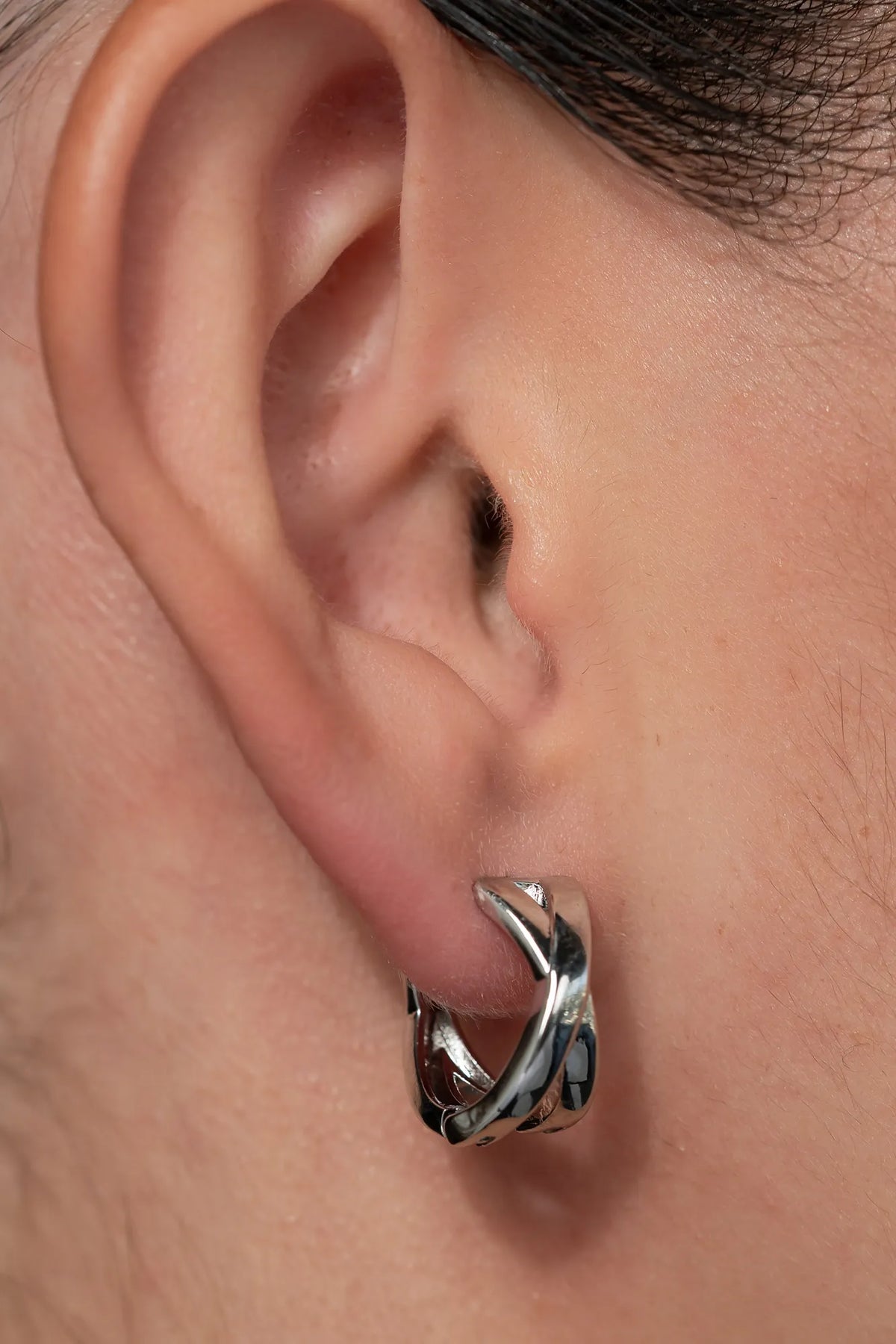 Model wearing silver-tone huggie earrings with a polished finish, sitting close to the earlobe.