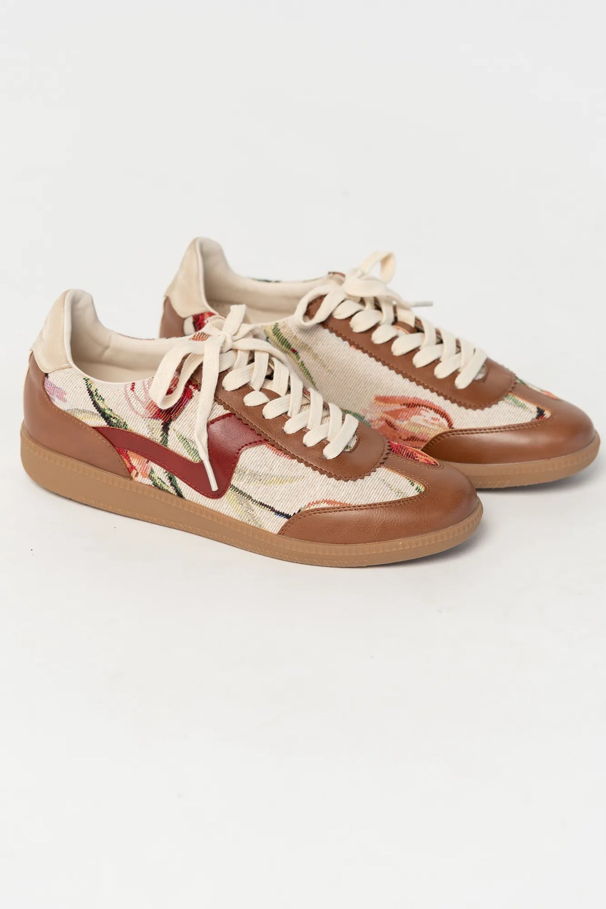 Pair of low-top sneakers  featuring cognac faux leather overlays, floral tapestry panels with rose motifs, and cream laces. The vintage-inspired design combines mixed textures and warm tones for a casual yet elevated everyday look.
