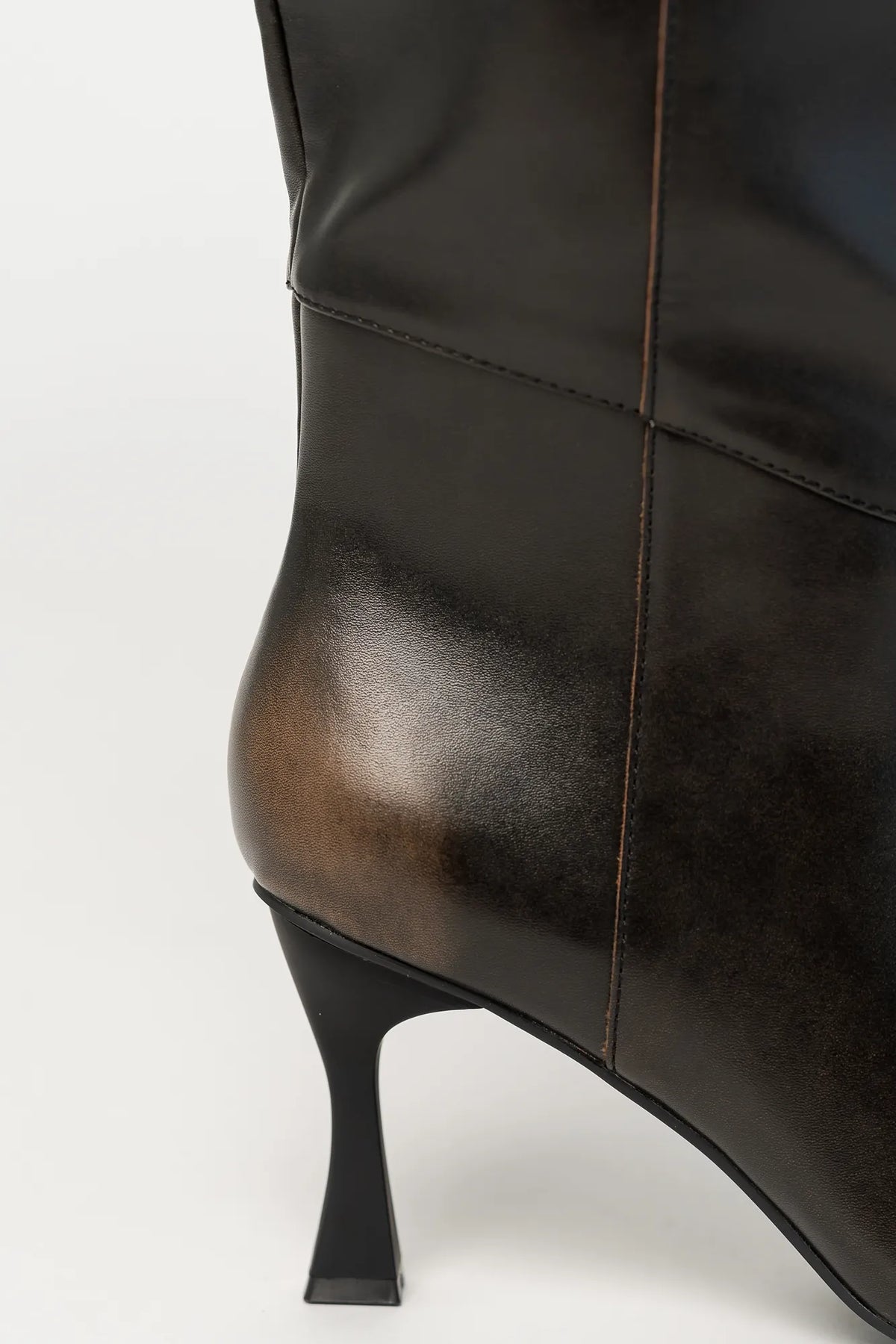 Close up of black knee-high boots featuring a sleek fitted shaft, and sculpted kitten heel. The streamlined silhouette and smooth finish create an elegant, versatile look that pairs effortlessly with dresses, skirts, and tailored outfits.