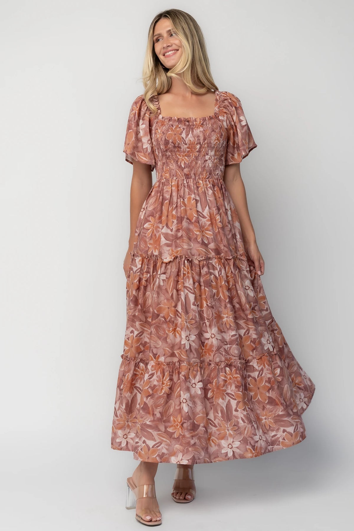 Model wearing the Southampton Smocked Maxi Dress in Dusty Mauve Floral featuring a square neckline, flutter sleeves with ruffle trim, a fully smocked bodice, and a flowing tiered maxi skirt with a dusty mauve floral print.