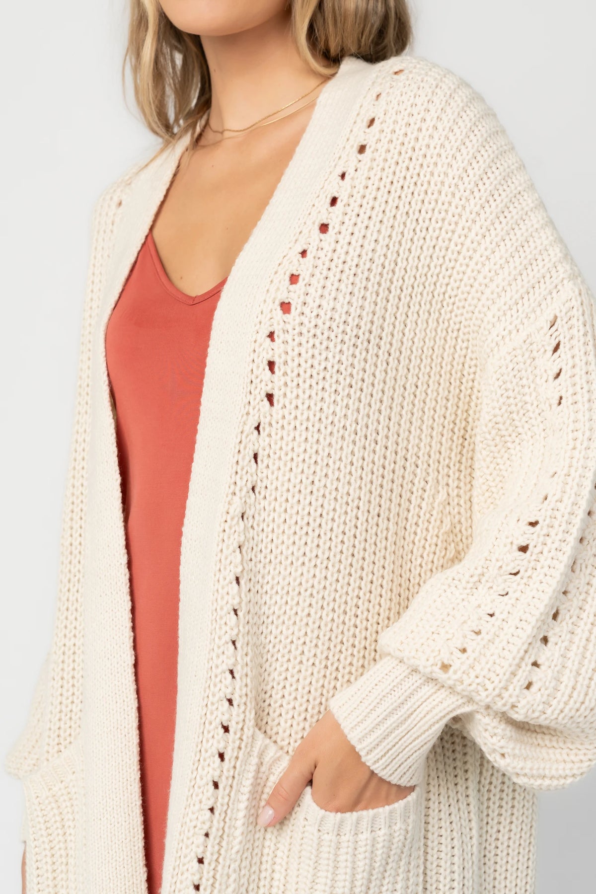 Natural chunky knit longline cardigan with an open front, pointelle detailing, balloon sleeves, ribbed trim, front patch pockets, and an oversized relaxed fit.