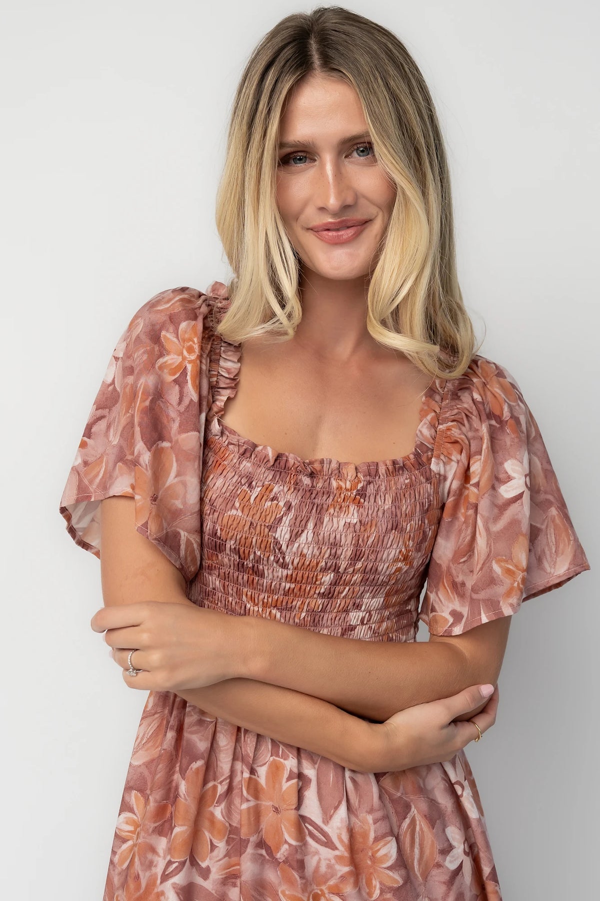 Model wearing the Southampton Smocked Maxi Dress in Dusty Mauve Floral featuring a square neckline, flutter sleeves with ruffle trim, a fully smocked bodice, and a flowing tiered maxi skirt with a dusty mauve floral print.