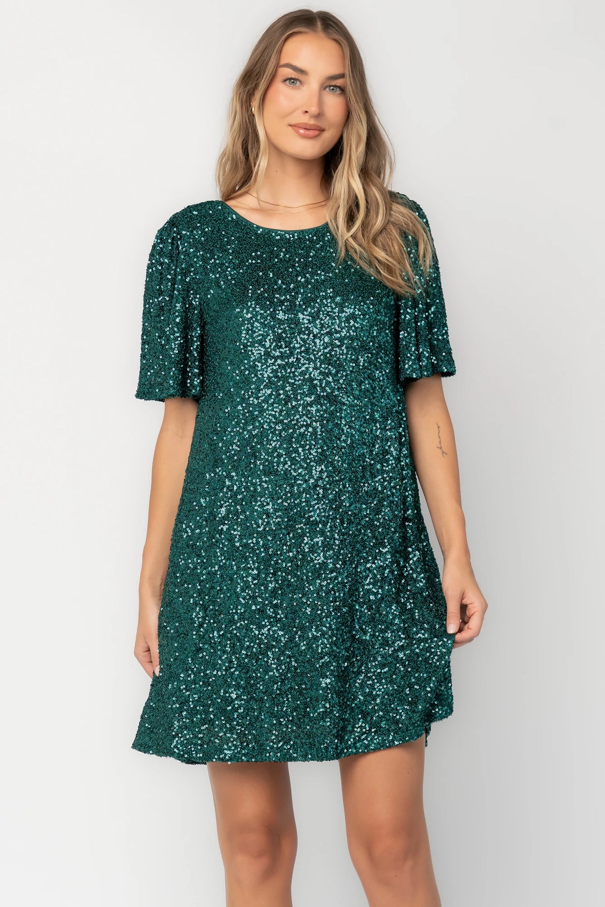 Emerald liquid sequin mini shift dress with a round neckline, short flutter sleeves, and a satin bow back detail.