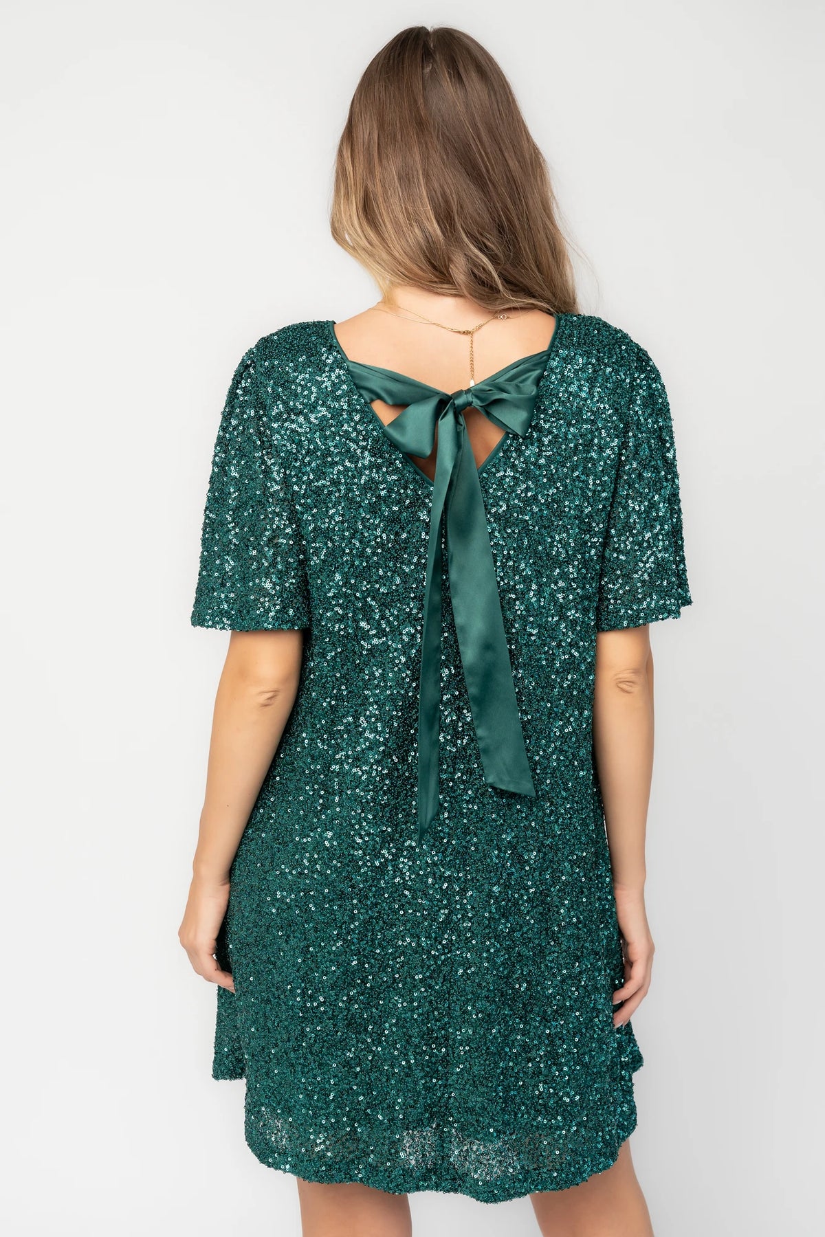 Emerald liquid sequin mini shift dress with a round neckline, short flutter sleeves, and a satin bow back detail.