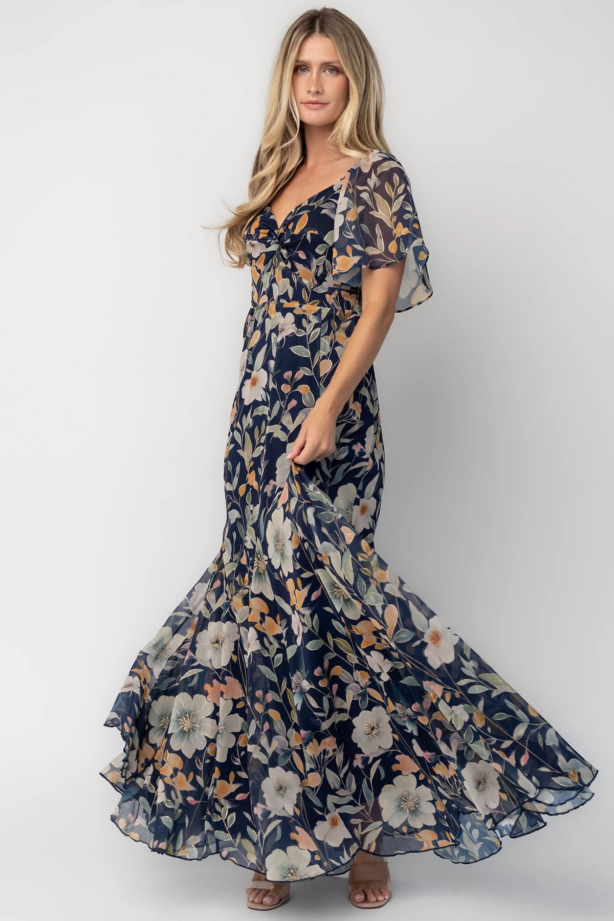 Navy floral chiffon maxi dress with a sweetheart neckline, knot detail, flutter sleeves, smocked back bodice, and a flowing tiered skirt.
