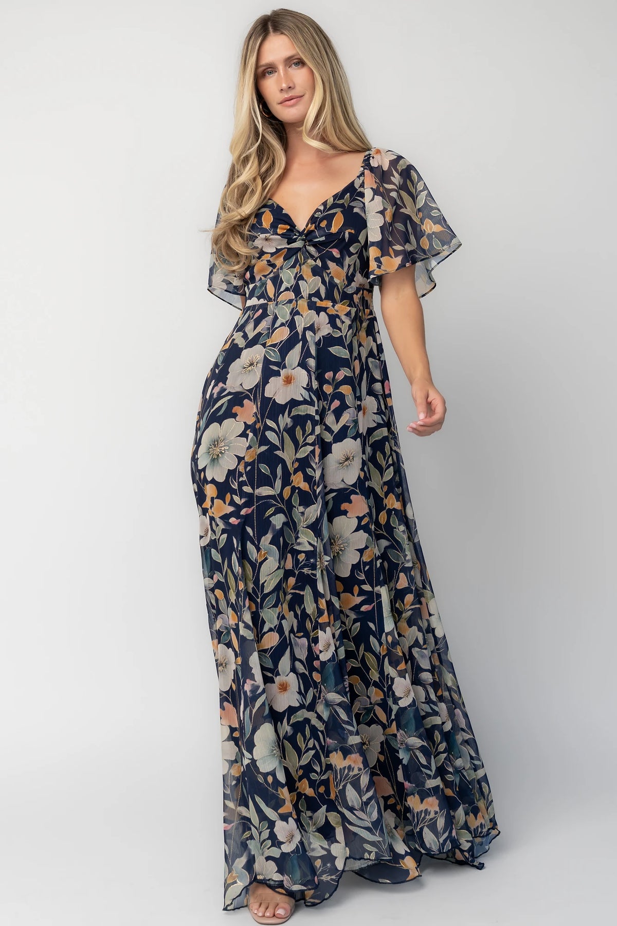 Navy floral chiffon maxi dress with a sweetheart neckline, knot detail, flutter sleeves, smocked back bodice, and a flowing tiered skirt.