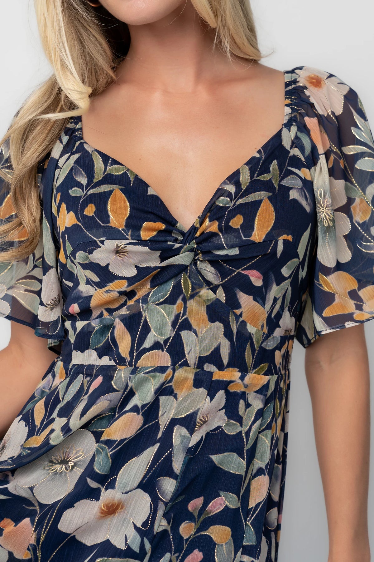 Navy floral chiffon maxi dress with a sweetheart neckline, knot detail, flutter sleeves, smocked back bodice, and a flowing tiered skirt.