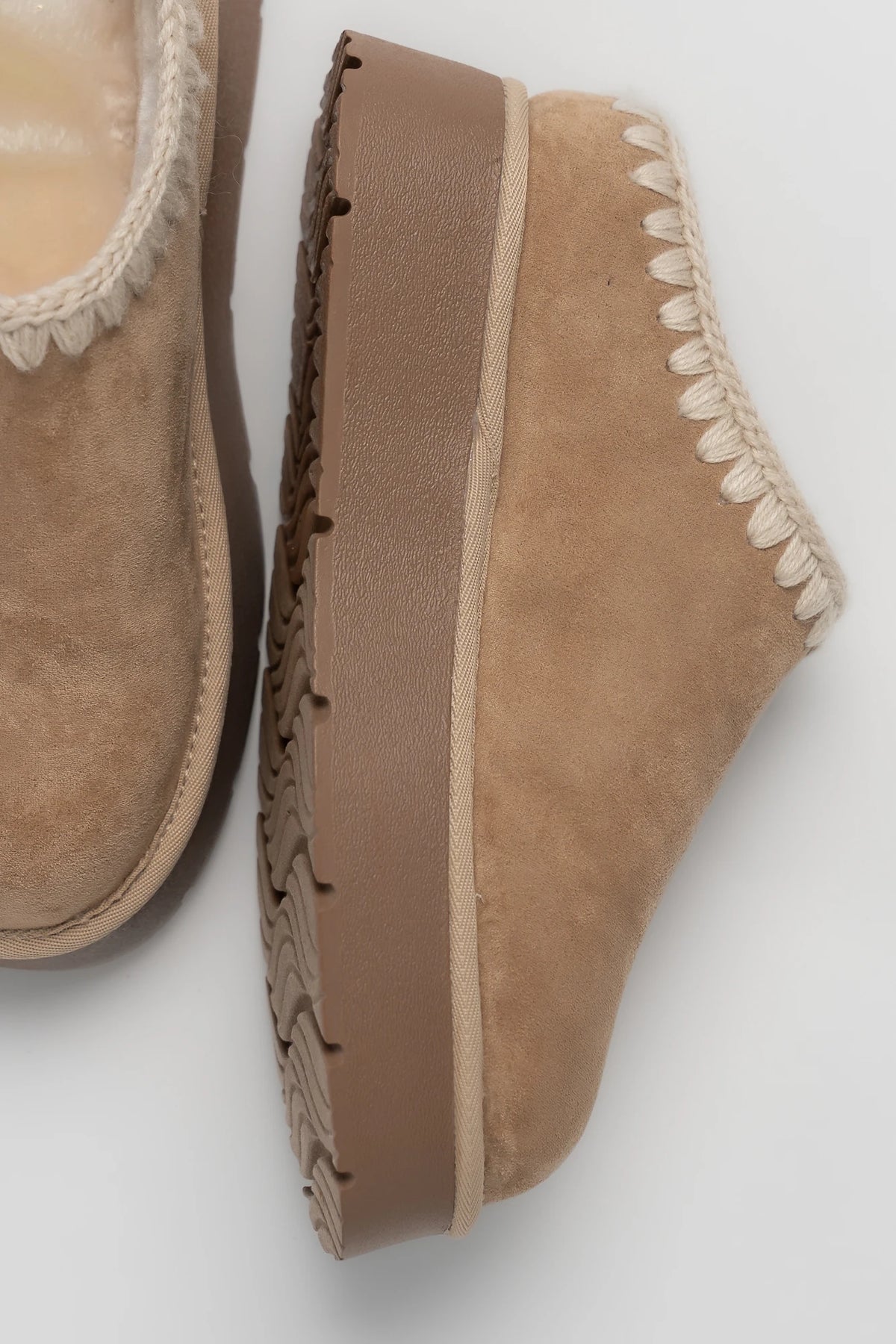 Tan platform mule slippers with a faux suede upper, plush faux fur lining, whipstitch trim, and cushioned slip-on design.