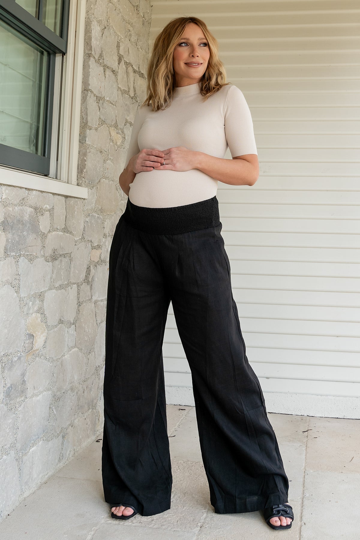 Model wearing Parvati smocked waist pants in black, side profile showing wide-leg silhouette and flowing linen-rayon fabric.