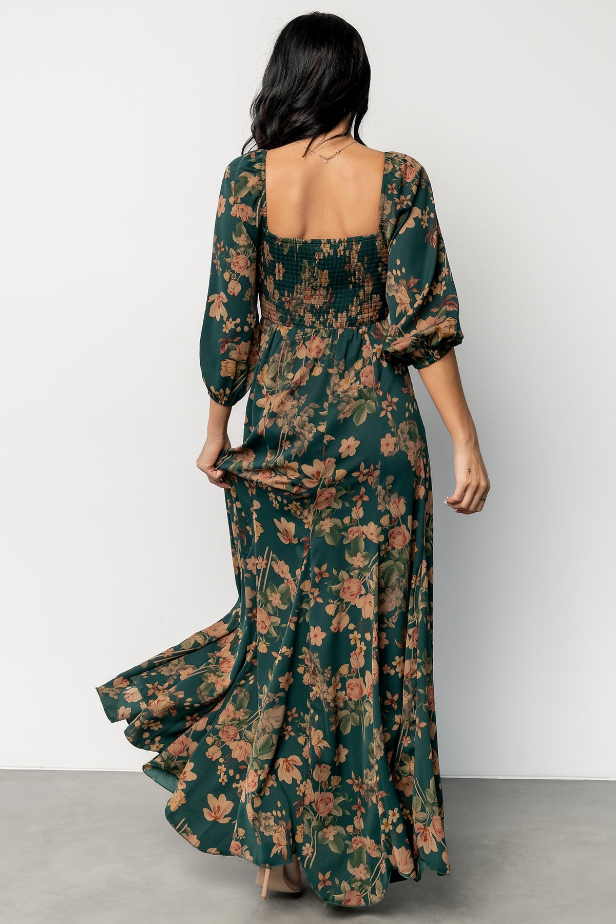 Model wearing green and copper floral maxi dress walking to show godet hem flare and hemline length.