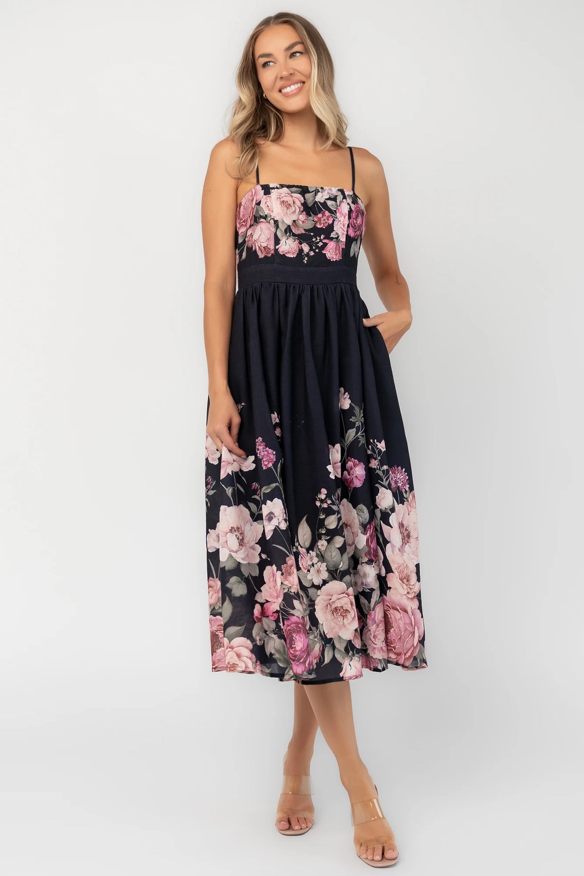 Black floral midi dress with a straight neckline, adjustable spaghetti straps, smocked back, gathered skirt, and side pockets.