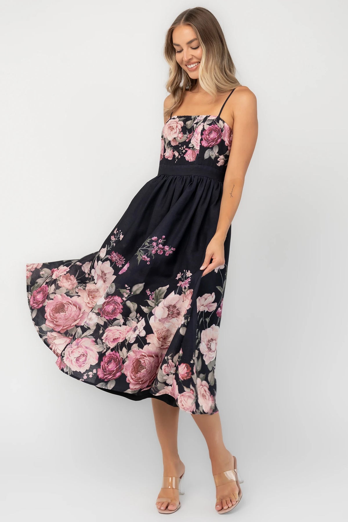 Black floral midi dress with a straight neckline, adjustable spaghetti straps, smocked back, gathered skirt, and side pockets.