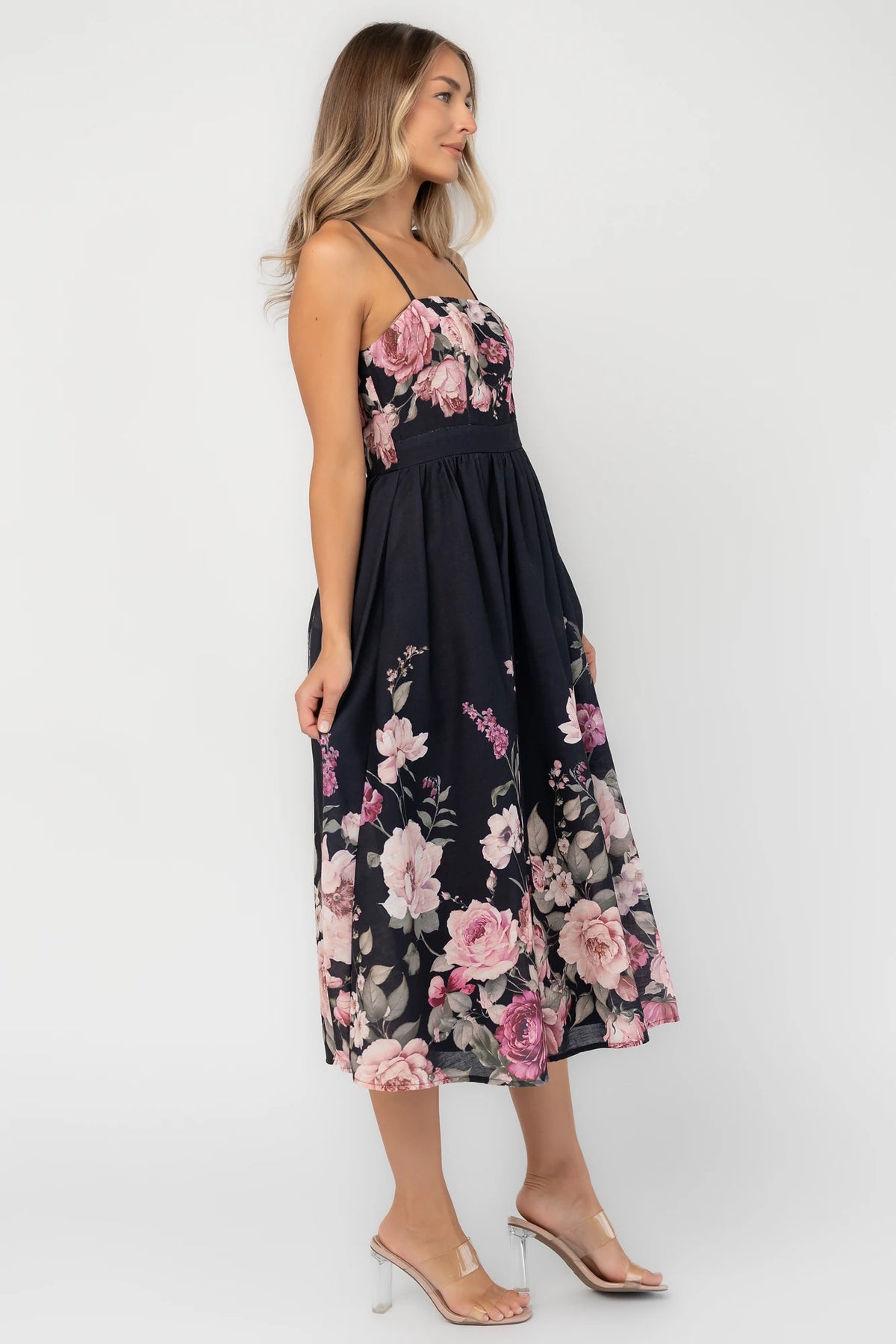 Black floral midi dress with a straight neckline, adjustable spaghetti straps, smocked back, gathered skirt, and side pockets.