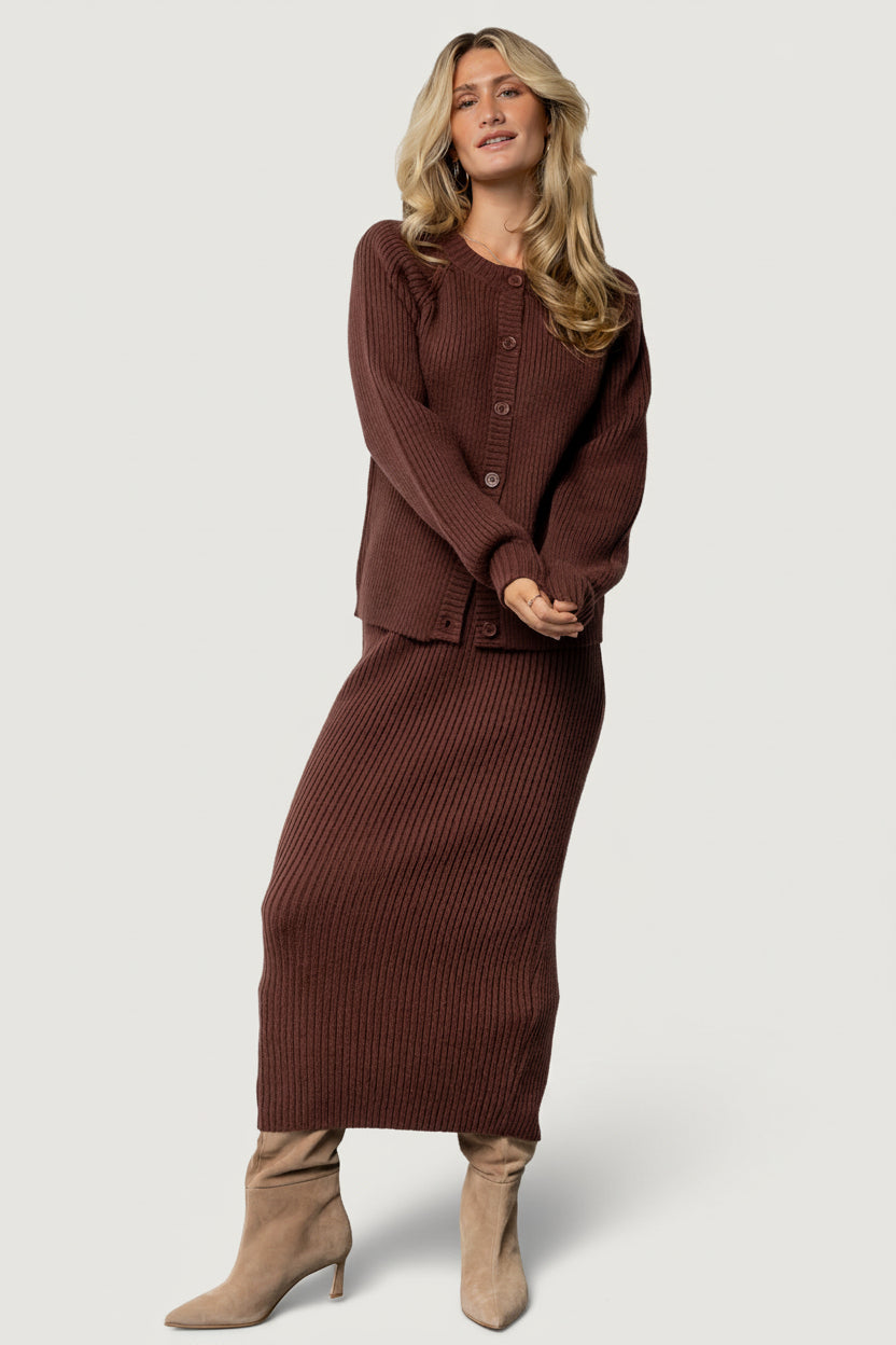 Close-up of mahogany ribbed knit fabric showing stitch detail, texture, and the raw hem edge of the skirt.