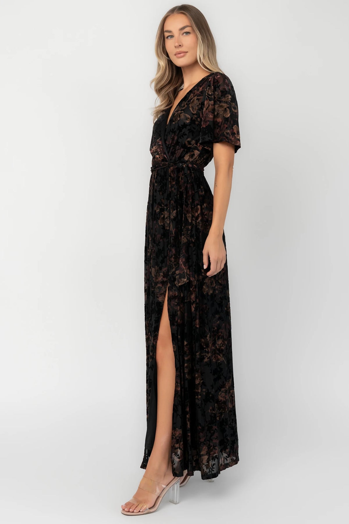 Bronze and black burnout velvet maxi dress with a surplice V-neckline, short flutter sleeves, elastic waist with a removable tie, and a flowing skirt with a side slit.
