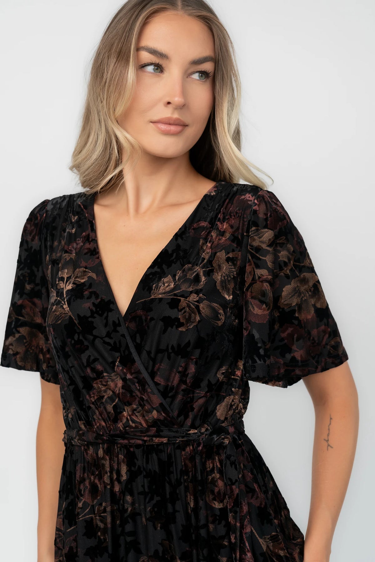 Bronze and black burnout velvet maxi dress with a surplice V-neckline, short flutter sleeves, elastic waist with a removable tie, and a flowing skirt with a side slit.