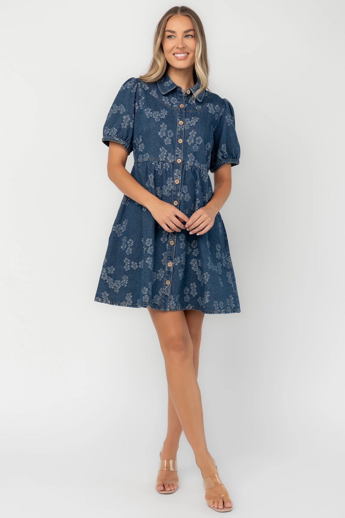 Medium wash floral denim mini dress with a collared neckline, button-front closure, short puff sleeves, empire waist, and side pockets.