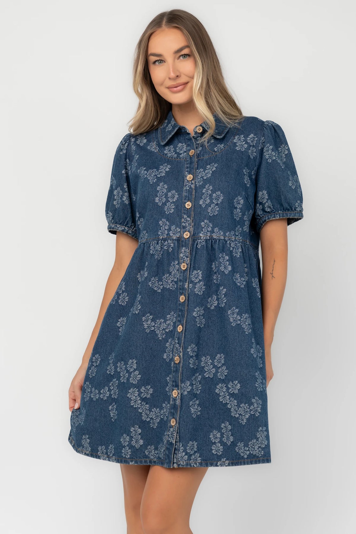 Medium wash floral denim mini dress with a collared neckline, button-front closure, short puff sleeves, empire waist, and side pockets.