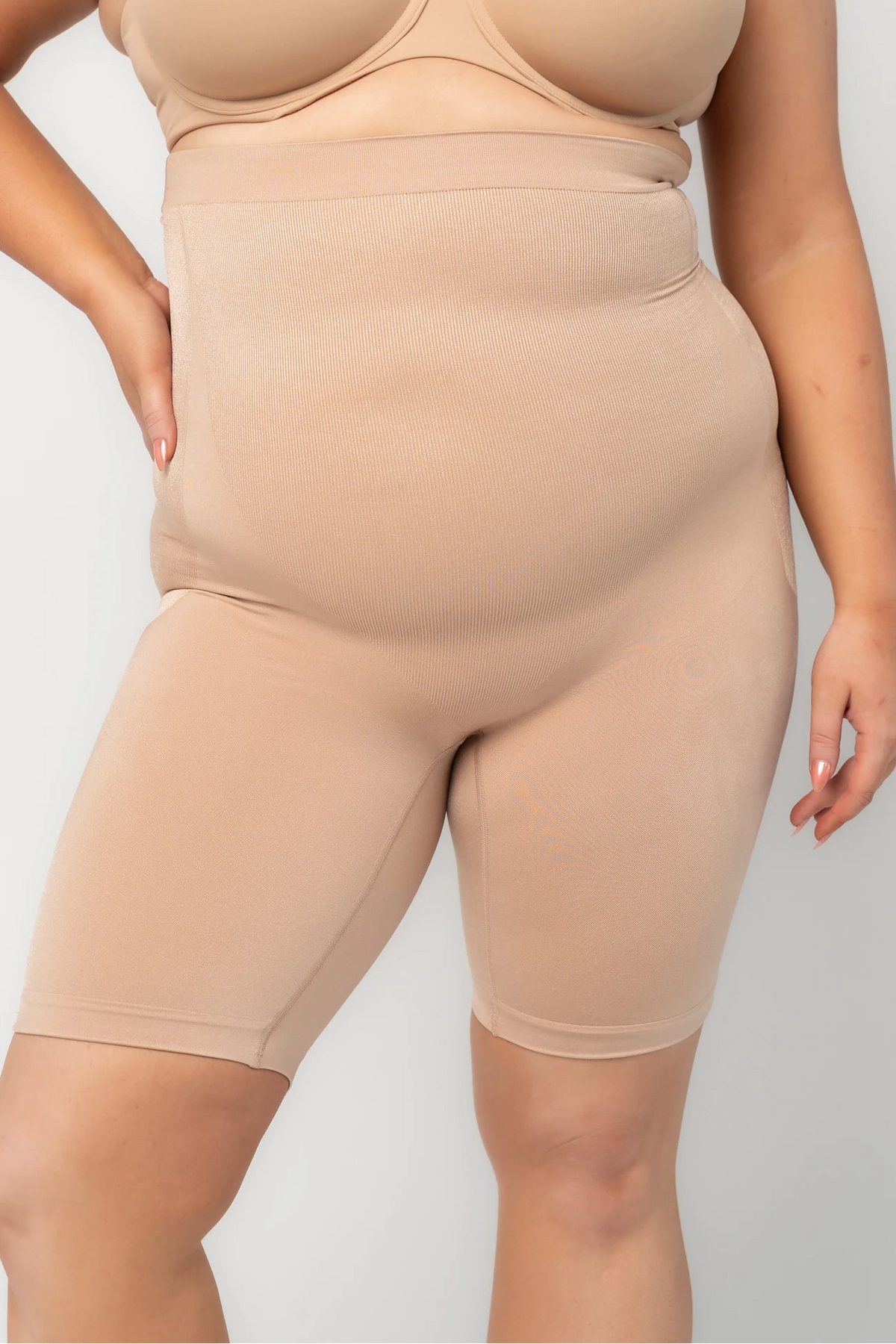 Model wearing nude high-waisted shaping shorts with a seamless design and mid-thigh length.