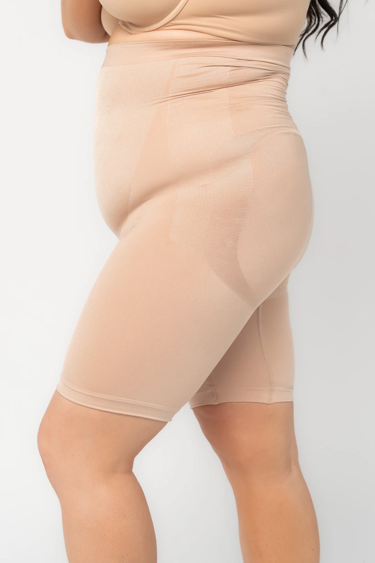 Model wearing nude high-waisted shaping shorts with a seamless design and mid-thigh length.