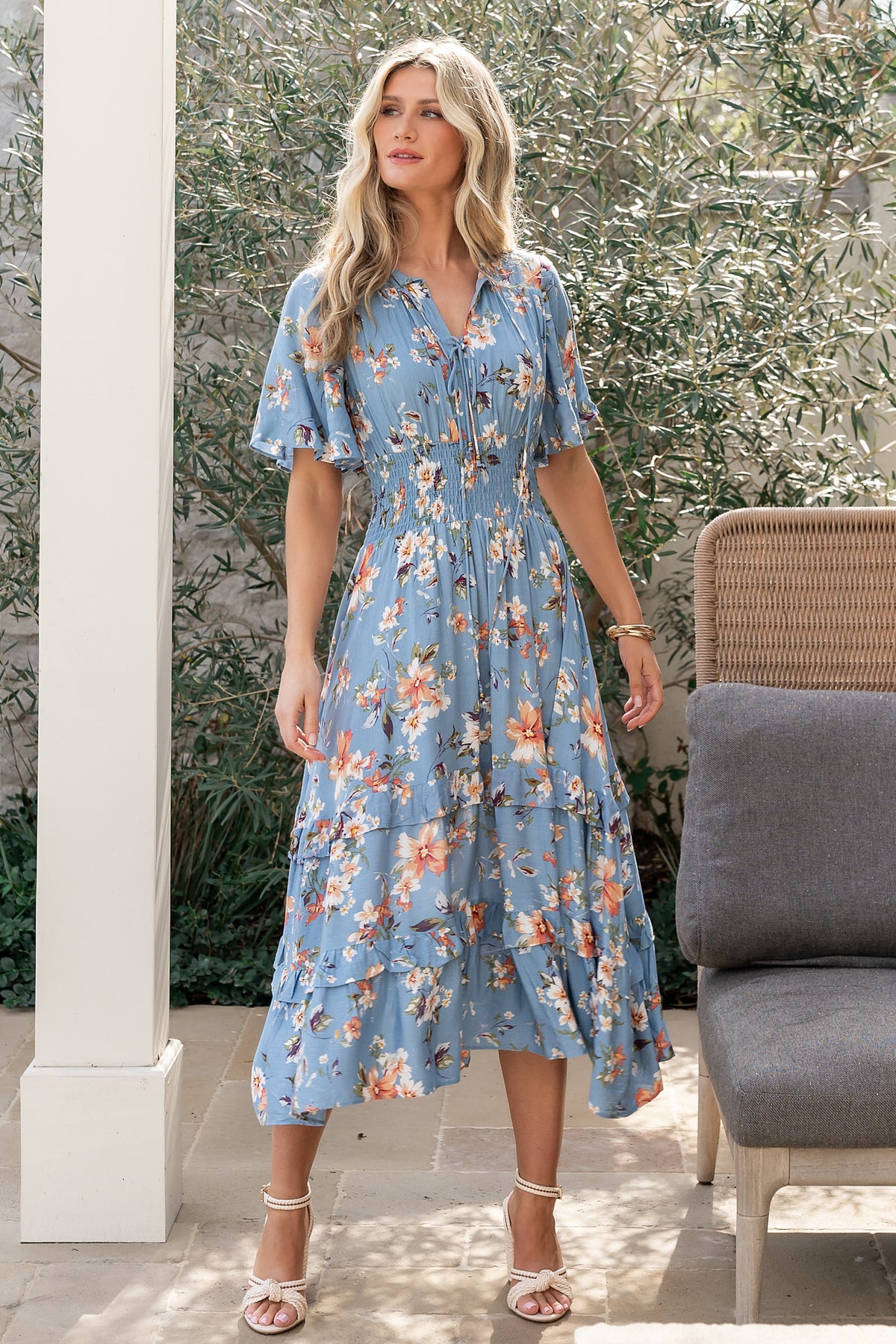 Front view of blue midi dress with peach floral print, V-neckline with ties, smocked waist, and lightweight rayon drape on model.
